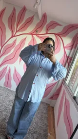 Camisa oversize de fibrana a rayas celestes y blancas, con cuello clásico, mangas largas con puños y botones frontales de acrílico en forma de corazón rojo.