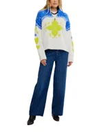 Sweater blanco con cuello alto y media cremallera, diseño holgado y extragrande. Presenta un patrón de punto jacquard en azul y amarillo neón, con motivos florales y geométricos. Los puños y el dobladillo son acanalados.