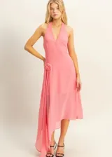 Vestido midi de color rosado con escote halter y espalda descubierta. Presenta un diseño asimétrico en el ruedo y un detalle de flor aplicada en la cintura.