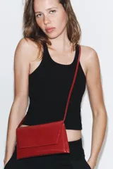 Bolso tipo bandolera de diseño estructurado, acabado brillante en color rojo y correa de cadena dorada. Cuenta con solapa frontal y doble compartimento interior.