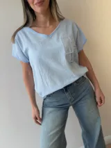 Remera celeste de lino y algodón, con escote en V, mangas cortas y calce relajado. Cuenta con estampa manuscrita, bolsillo decorativo con strass, encaje, tachas y detalles desflecados.