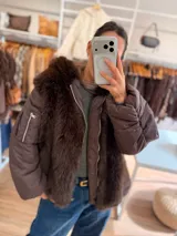 Campera puffer oversize color marrón, con paneles frontales y traseros de pelo sintético suave. Presenta mangas acolchadas, cierre frontal y bolsillo con cierre en la manga.