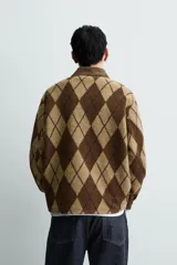 Polo de corte relajado confeccionada en tejido de textura con diseño de rombos en tonos marrones. Presenta cuello de solapa en pana, cierre frontal con botones, mangas largas con puños abotonados y bordado a contraste en el pecho.