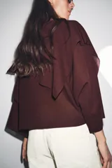 Jersey de punto color vino tinto, de corte amplio y holgado, con cuello bote y un detalle de capa asimétrica superpuesta en la parte superior delantera. Mangas anchas tipo murciélago.