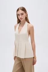 Blusa de algodón color beige con escote en V, cuello halter y cierre frontal con botones. Presenta un diseño ajustado en el torso con pinzas y pliegues en la parte inferior que generan una caída ligeramente acampanada.