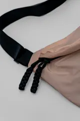 Bandolera de diseño minimalista en color beige, con correa ajustable negra y cierre frontal con tiradores de cordón.