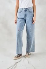 Pantalón de jean celeste de corte ancho, con bordados verticales de líneas rojas, blancas y azules.