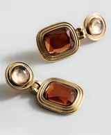 Pendientes colgantes dorados con diseño articulado, compuesto por una pieza superior circular abombada y un colgante rectangular inferior con una piedra de cristal marrón facetada y marco texturizado con líneas concéntricas.