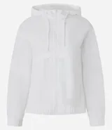 Campera deportiva cortaviento color blanco, con capucha ajustable, cierre frontal por cremallera y diseño de corte holgado. Incluye saquito para guardar.