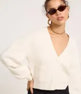 Cardigan corto de punto color beige claro, con escote en V, manga larga abullonada y cierre frontal de botones. Posee bolsillos delanteros tipo parche.