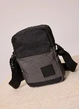 Bandolera Rusty Garin de color gris oscuro y negro, con cierre superior, bolsillo frontal y correa ajustable.