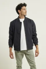 Campera tipo bomber color verde militar, confeccionada en 100% algodón. Cuenta con puños tejidos al tono, cuello y cintura elásticos, y cierre frontal metálico.