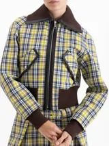 Chaqueta cropped de tela cuadrillé en tonos verde, amarillo y azul. Presenta cuello, puños y ruedo en tejido ribb color chocolate, cierre frontal con cremallera, bolsillos con tapa y detalles en cuero sintético.