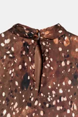 Vestido corto de cuello redondo y manga larga, con diseño de volantes superpuestos en el frente. Presenta un estampado abstracto en tonos marrones y cierre en la espalda con abertura y botones.