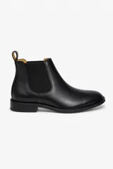 Botín tipo Chelsea de cuero negro con paneles laterales elásticos y tirador en la parte trasera. Diseño clásico con suela plana y tacón bajo.