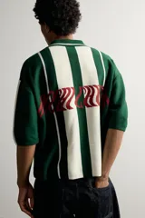 Polo de punto boxy fit color verde oscuro y blanco, de manga corta, con cuello solapa, cierre frontal con botones y detalle de texto bordado a contraste en el pecho.