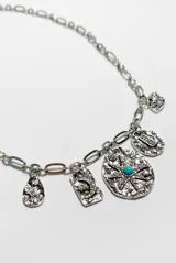 Collar dorado de cadena eslabonada con múltiples dijes colgantes texturizados, adornados con pedrería y una piedra central de color turquesa.