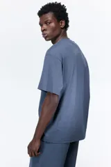 Remera de algodón de peso medio, color azul, con cuello redondo ribeteado, hombros caídos y corte relajado.