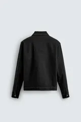 Sobrecamisa de denim de algodón negro con efecto lavado, corte relajado (relaxed fit). Presenta cuello solapa, cierre frontal con cremallera, manga larga con puño abotonado y bolsillo plastrón en el pecho.