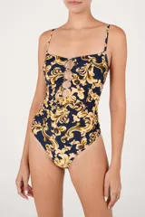 Malla enteriza de color azul marino con estampado barroco en tonos beige y dorado. Presenta un escote recto con tirantes finos, aberturas frontales unidas por argollas metálicas y laterales fruncidos.
