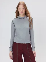 Polera de cuello alto confeccionada en tela rib color blanco, con mangas largas y hombreras. Presenta pespuntes en contraste en las terminaciones del cuello, hombros y puños.