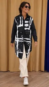 Camisa larga tipo vestido de corte oversize, con diseño artístico en blanco y negro. Presenta detalles de flecos en los hombros, apliques decorativos y cierre frontal con botones.