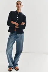 Chaqueta de punto color negro con cuello redondo, manga larga y cierre frontal con botones dorados. Presenta un corte entallado con bajo en evasé.