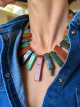 Collar corto elaborado con piedras rectangulares en tonos verdes, naranjas y grises oscuros, unidas con herrajes dorados y cadena de eslabones con dije colgante.
