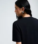 Remera negra de algodón con cuello redondo y mangas cortas. Presenta un estampado gráfico frontal con la imagen de la cantante Jennie y la inscripción 'Jennie Ruby' junto al texto 'Act 1, Stage 2 Curiosity'.