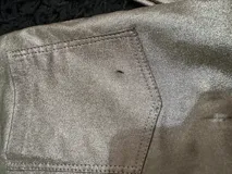 Pantalón de tiro alto confeccionado en eco cuero con acabado metalizado dorado. Presenta un corte recto con aberturas laterales con cierre en los tobillos y costuras frontales decorativas.