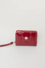 Billetera de cuero con textura tipo cocodrilo, color marrón, con cierre perimetral y solapa frontal con broche a presión metálico. Incluye una correa de muñeca desmontable.