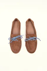 Mocasín tipo boat shoe color marrón, confeccionado en cuero, con cordones de cuero marrón y cordones decorativos azules.