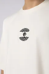 Remera de corte oversize confeccionada en algodón premium de gramaje pesado, color crudo. Presenta un bordado frontal pequeño en el centro del pecho con un diseño de dos árboles unidos por sus raíces y un parche estampado en la espalda con una silueta de mano fusionada con ramas.