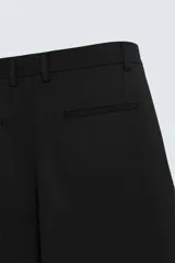 Bermuda de corte relajado color gris, con pliegues frontales, cierre de cremallera y botón, bolsillos laterales y bolsillos traseros tipo plastrón.