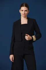 Saco corto tipo blazer color negro, de corte entallado y manga larga. Presenta un detalle distintivo en el puño izquierdo con una banda en tono dorado que incluye la inscripción 'ANTOLIN'.