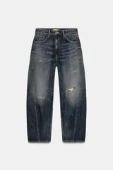 Jeans de tiro medio con diseño baggy balloon, cinco bolsillos y costuras laterales torcidas. Presenta un acabado desgastado con roturas localizadas y cierre frontal con cremallera y botón metálico.