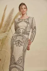 Vestido largo de fiesta color beige, con mangas largas y cuello redondo. Presenta un intrincado diseño bordado con canutillos y lentejuelas en tonos plata y gris, creando patrones geométricos y ornamentales en toda la prenda.