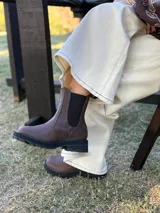 Bota tipo Chelsea de cuero color chocolate, con paneles elásticos laterales y suela track dentada de goma negra.