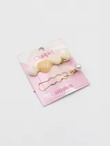 Set de dos broches para el pelo en tono dorado. Uno de los broches presenta tres corazones de resina en tonos crema y beige, mientras que el otro tiene un diseño ondulado con una perla blanca en el extremo.