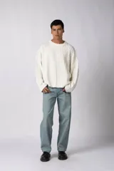 Sweater de punto color blanco con diseño asimétrico, presentando una mitad lisa y la otra mitad con textura de trenzas verticales. Posee cuello redondo y mangas largas con terminación en puño.