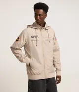 Campera rompevientos color beige con capucha, cierre frontal y bolsillos con cremallera. Presenta estampa de la NASA en el pecho, parches en las mangas y puños elastizados.
