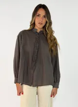 Camisa de corte oversize y diseño holgado, con cuello camisero, cierre frontal de botones y mangas largas con puños abotonados. Presenta un ruedo redondeado y una caída fluida.