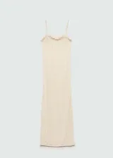 Vestido largo de punto calado en color crema, con tirantes finos, escote recto y terminaciones con volantes delicados. Presenta un diseño entallado que se ajusta a la silueta.