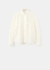 Blusa de tejido semitransparente color crudo, con diseño recto, cuello alto con volados, mangas largas abullonadas con puños abotonados y detalle de bordado floral en toda la prenda. Cuenta con cierre frontal de botones ocultos y ribete con volado en la botonera.