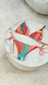 Conjunto de bikini reversible con diseño de bloques de colores abstractos. El top es de estilo triangular con tiras para atar y detalle de argollas metálicas. La bombacha es de corte vedetina, con tiras laterales para atar y detalle de argollas.