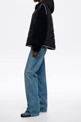 Chaleco acolchado color crema con capucha integrada, cierre frontal de botones a presión y vivos en contraste color negro. Presenta diseño de costuras geométricas y bolsillos laterales.