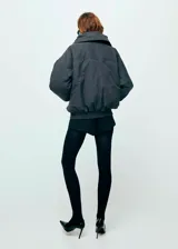 Chaqueta estilo bomber color negro, de corte oversize, con cuello alto amplio, cierre frontal de cremallera metálica y bolsillos laterales.