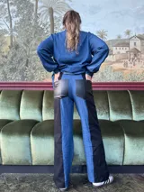 Pantalón de tiro alto con pierna ancha, confeccionado en denim azul y cuerina negra.