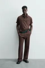 Polo de hombre de corte relajado, color marrón oscuro, confeccionado en tejido texturizado con rayas verticales. Posee cuello solapa y cierre frontal con botonadura oculta por solapa.