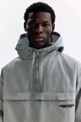 Campera popover de algodón color gris con efecto lavado, cuello elevado, capucha con cordón ajustable, medio cierre y bolsillo frontal con solapa.